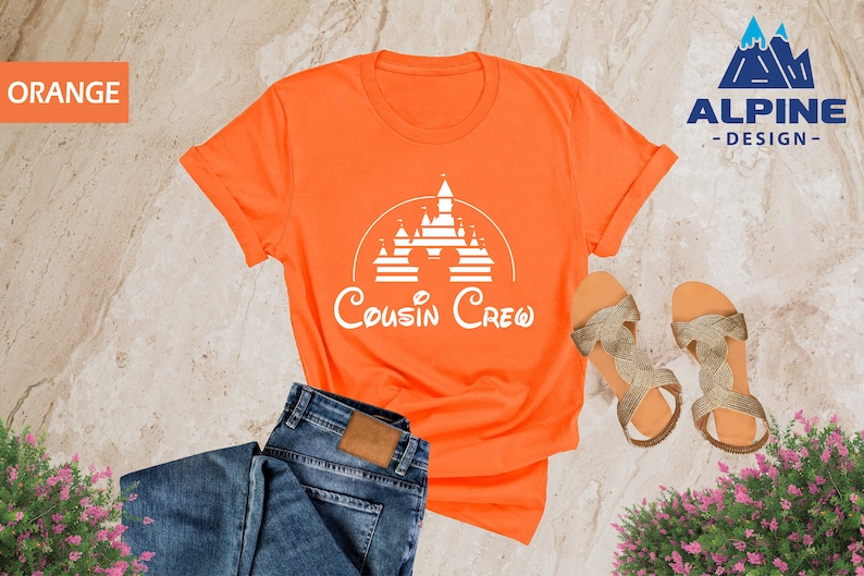 Pode incluir: Camiseta laranja com um gr&aacute;fico branco de um castelo e o texto "Cousin Crew".