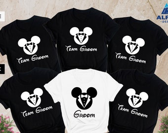 May include: Six t-shirts with a Mickey Mouse design wearing a tuxedo. The shirts are black and white with the text "Team Groom" and "Groom" printed on them.
