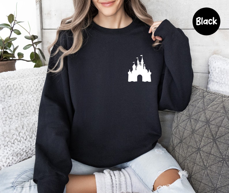 Op de afbeelding: Een zwart sweatshirt met een wit silhouet van Assepoester's kasteel op de voorkant. Het sweatshirt is een ronde hals en heeft lange mouwen.