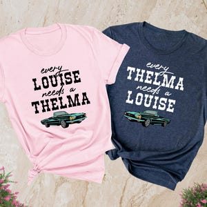 May include: Two t-shirts, one pink and one heather navy, with a vintage car graphic and text that reads "every LOUISE needs a THELMA" and "every THELMA needs a LOUISE".