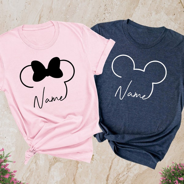 May include: Two t-shirts, one pink and one heather navy, with a Mickey Mouse silhouette design. The pink shirt has a bow on the silhouette and the navy shirt has a white outline. Both shirts say "Name" underneath the silhouette.