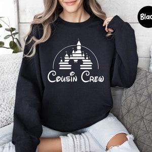 Pode incluir: Camisola de cor preta com um gr&aacute;fico branco de um castelo da Disney e o texto "Cousin Crew".