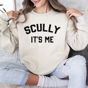 May include: A sand-colored sweatshirt with the text "SCULLY IT'S ME" in black.
