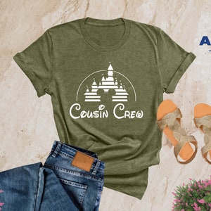 Pode incluir: Uma camiseta verde oliva heather com um gr&aacute;fico branco de um castelo e o texto "Cousin Crew".
