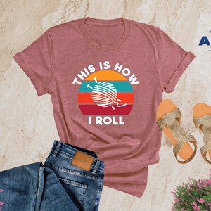 May include: Heather mauve t-shirt with a retro sunset graphic and the text "This is how I roll" with a yarn ball and knitting needles in the center of the graphic.