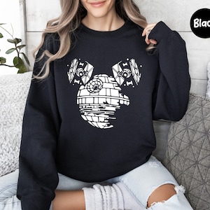 May include: Black sweatshirt with a white graphic of the Death Star from Star Wars, with two TIE fighters on either side of the Death Star, forming a Mickey Mouse silhouette.