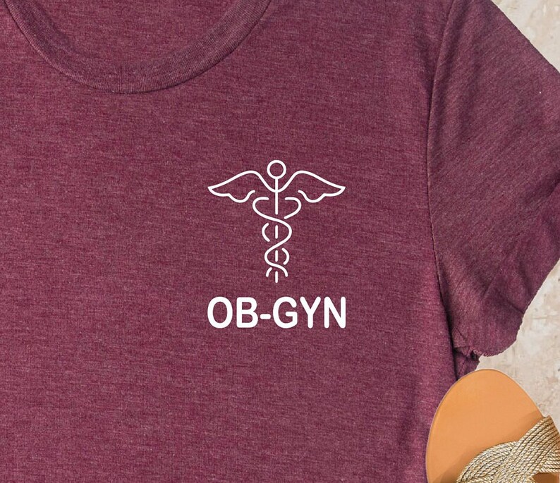 May include: A maroon t-shirt with a white outline of a medical caduceus symbol and the text "OB-GYN".
