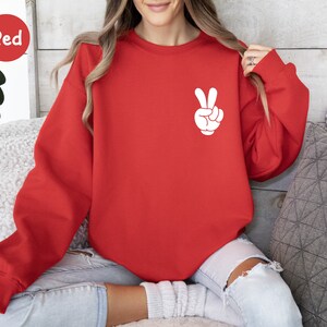 May include: Red sweatshirt with a white peace sign graphic on the front.