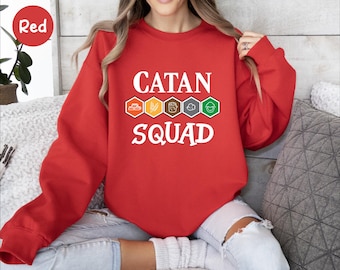 May include: Red sweatshirt with white text that reads "CATAN SQUAD" and five small icons representing the Catan game resources.