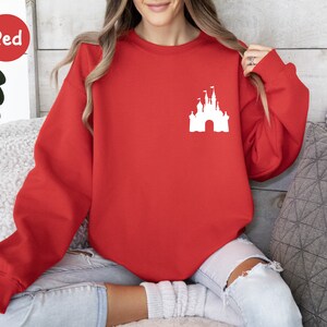 Op de afbeelding: Rood sweatshirt met een wit silhouet van Assepoester's kasteel op de voorkant.