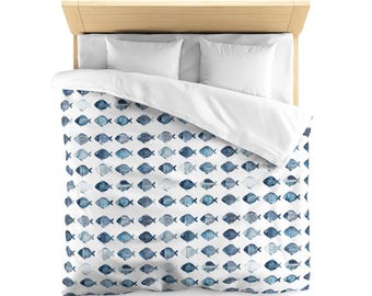 May include: A bed with a light wood frame, white pillows, and a white duvet cover. The duvet features a pattern of blue fish in various designs on a white background. The bed is made up and ready for use.