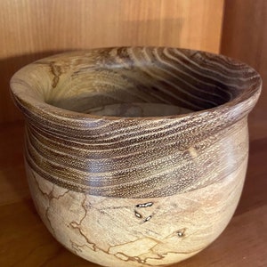 May include: A wooden bowl with a dark brown top and a light brown bottom. The bowl has a unique grain pattern and is made of natural wood.
