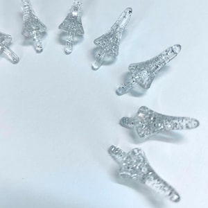 May include: A group of clear plastic Christmas tree toppers with silver glitter. The toppers are shaped like a Christmas tree and have a pointed top.