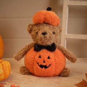 May include: A plush teddy bear with brown fur wearing a black bow tie and a bright orange pumpkin hat. The bear is attached to a round, fuzzy orange pumpkin body featuring a stitched black jack-o'-lantern face with triangular eyes and a grin.