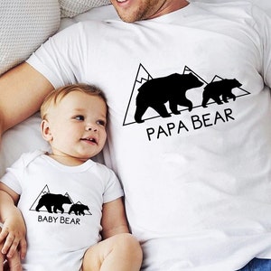 May include: A white t-shirt with a black bear silhouette and the text "Papa Bear" and a smaller bear silhouette with the text "Baby Bear".