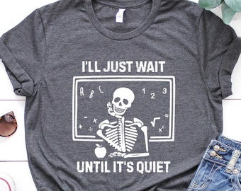 May include: A dark gray t-shirt with a white graphic of a skeleton sitting at a chalkboard with the text "I'll just wait until it's quiet".