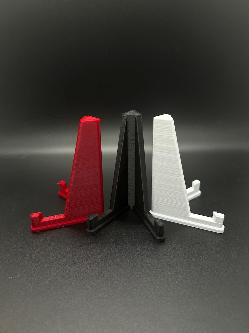 May include: Three triangular display stands made of plastic. The stands are red, black, and white.