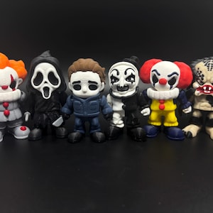 Pode incluir: Um conjunto de seis figuras de personagens de filmes de terror. As figuras est&atilde;o todas em posi&ccedil;&atilde;o de p&eacute; e s&atilde;o feitas de pl&aacute;stico. Os personagens incluem Pennywise o palha&ccedil;o, Ghostface, Michael Myers, Art o palha&ccedil;o, Predator e uma figura mascarada.