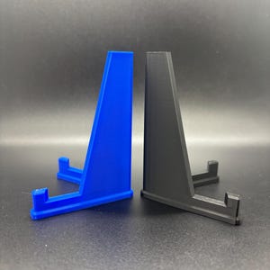 May include: Two display stands, one blue and one black, made of plastic. The stands are shaped like a triangle with a small platform at the top.