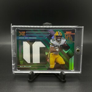 May include: Green Bay Packers rookie football card featuring AJ Dillon. The card is a green, black, and white design with a holographic finish. The card number is 2/5.