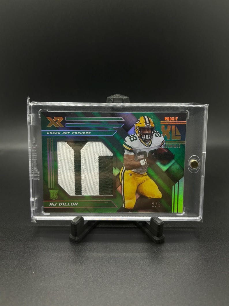 May include: Green Bay Packers rookie football card featuring AJ Dillon. The card is a green, black, and white design with a holographic finish. The card number is 2/5.