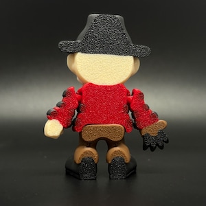 Pode incluir: Uma figura de brinquedo articulada de cor vermelha e marrom que representa uma pessoa com um chap&eacute;u de caub&oacute;i preto. A figura est&aacute; de p&eacute; com os bra&ccedil;os estendidos.