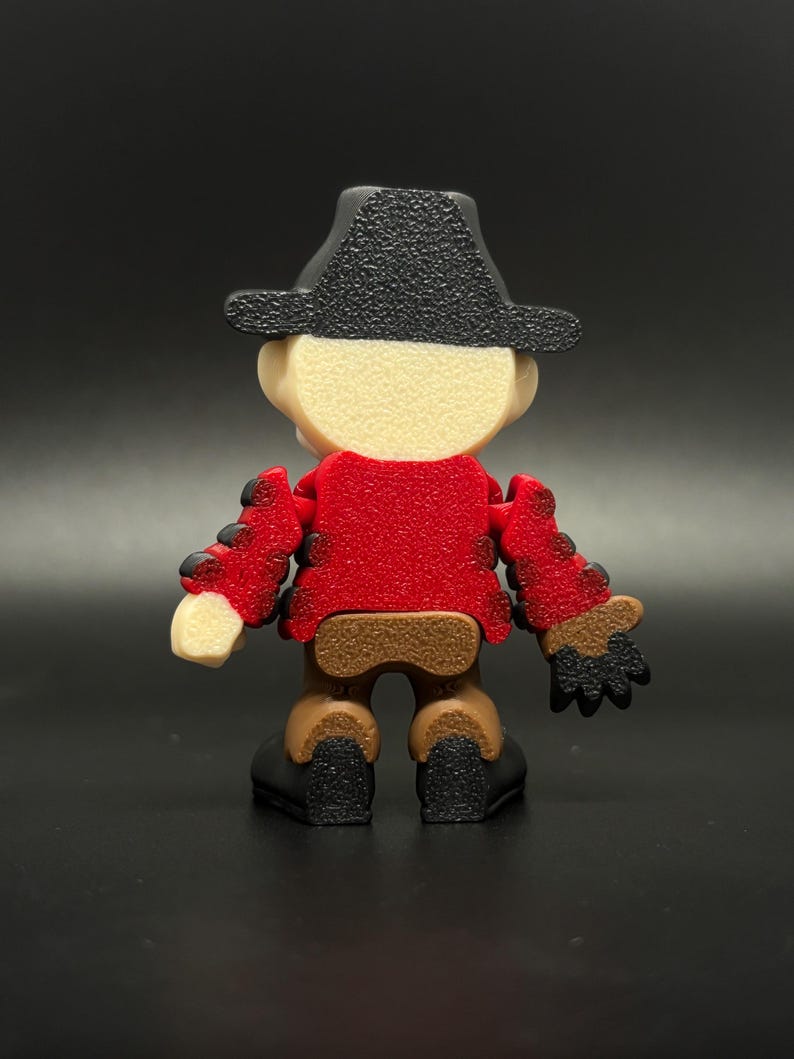 Pode incluir: Uma figura de brinquedo articulada de cor vermelha e marrom que representa uma pessoa com um chap&eacute;u de caub&oacute;i preto. A figura est&aacute; de p&eacute; com os bra&ccedil;os estendidos.