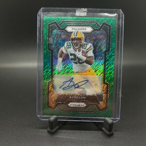 May include: Green, gold and silver football trading card featuring a player in a green and gold uniform with the text "PACKERS" and "AJ DILLON" on the card. The card is a Prizm card.