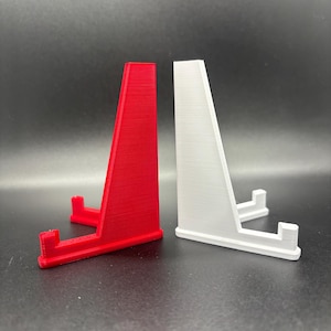 May include: Two display stands, one red and one white, made of plastic. The stands are designed to hold small objects, such as figurines or jewellery.