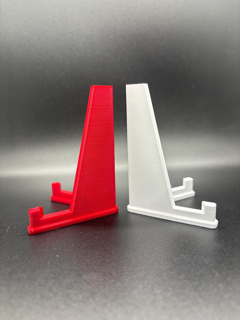 May include: Two display stands, one red and one white, made of plastic. The stands are designed to hold small objects, such as figurines or jewellery.
