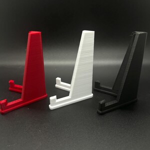 May include: Three plastic display stands, one red, one white and one black. The stands are angled and have a small platform at the top.