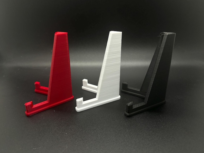 May include: Three plastic display stands, one red, one white and one black. The stands are angled and have a small platform at the top.