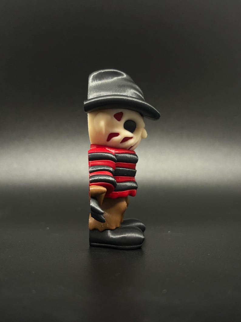 Pode incluir: Uma figura de Freddy Krueger com listras vermelhas e pretas, um chap&eacute;u preto e um rosto castanho. A figura &eacute; feita de pl&aacute;stico e tem cerca de 7,5 cm de altura.