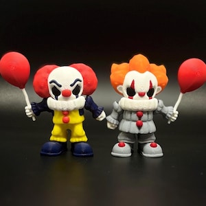 May include: Two small clown figurines, one in yellow and the other in gray, each holding a red balloon. The clowns have white faces with black eye markings and red noses. The background is a solid black.