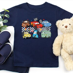 May include: A navy blue t-shirt with a graphic of cartoon cars racing on a checkered flag background. The cars are red, blue, green, and yellow.