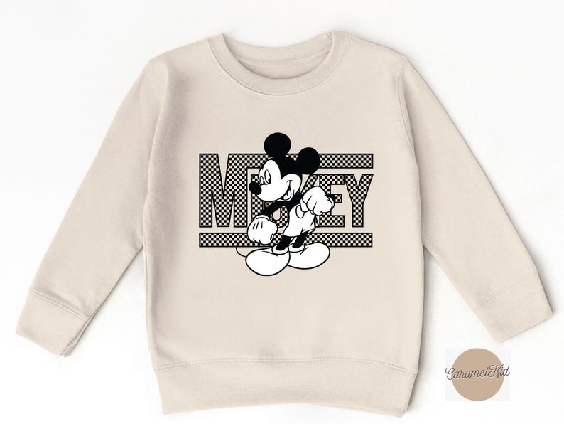 May include: A beige sweatshirt with a black and white graphic of Mickey Mouse and the word "Mickey" in a checkered pattern.