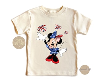 May include: A white t-shirt with a red, white, and blue Minnie Mouse graphic. Minnie Mouse is wearing a red bow and a blue dress with white stars. There are red, white, and blue fireworks around her.