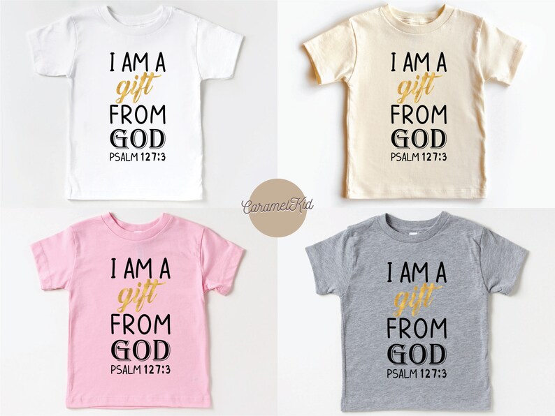 Op de afbeelding: Vier T-shirts in kindermaat in wit, beige, roze en grijs met de tekst "I AM A gift FROM GOD PSALM 127:3" gedrukt in zwart en goud.