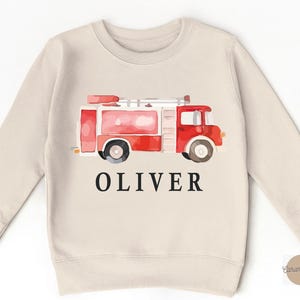 May include: A beige sweatshirt with a watercolor illustration of a red fire truck and the name "Oliver" printed on the front.