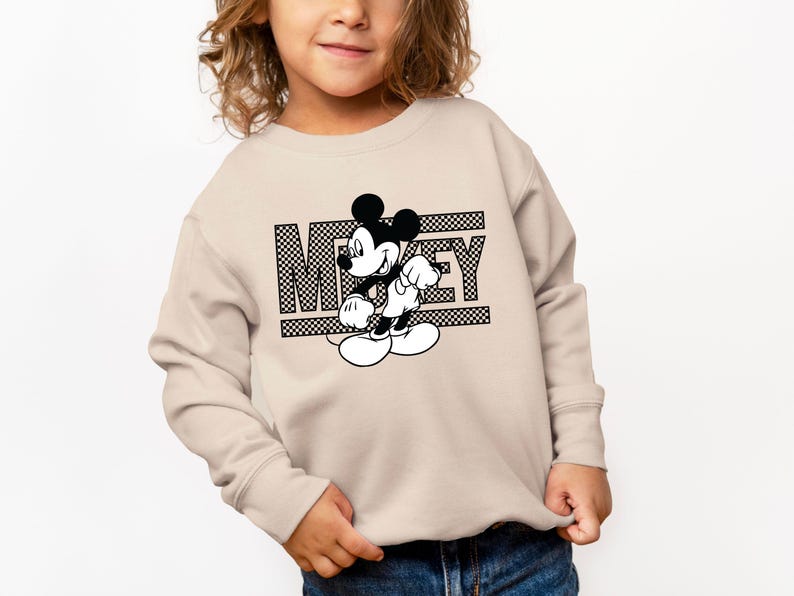 May include: A beige sweatshirt with a black and white graphic of Mickey Mouse and the word "Mickey" printed on the front.