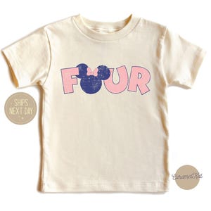 K&ouml;nnte beinhalten: Ein hellbeiges T-Shirt mit einer pinkfarbenen und blauen Grafik, auf der "FOUR" steht, mit einem blauen Mickey-Maus-Kopf mit einer pinkfarbenen Schleife.