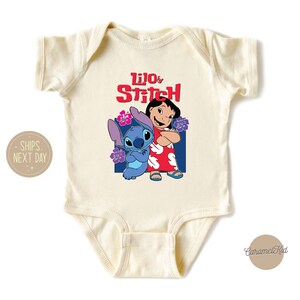 May include: A cream-colored baby onesie with a graphic of Lilo and Stitch from the Disney movie Lilo & Stitch. The text "Lilo & Stitch" is printed in red letters above the characters.