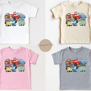 May include: Four different colored t-shirts featuring a cartoon image of a group of cars from the Cars movie. The cars are on a checkered flag background. The t-shirts are white, beige, pink, and gray.