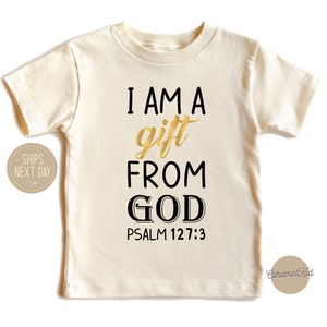 Op de afbeelding: Een cr&egrave;mekleurig T-shirt met korte mouwen en de tekst "I AM A gift FROM GOD PSALM 127:3" gedrukt in zwart en goud.