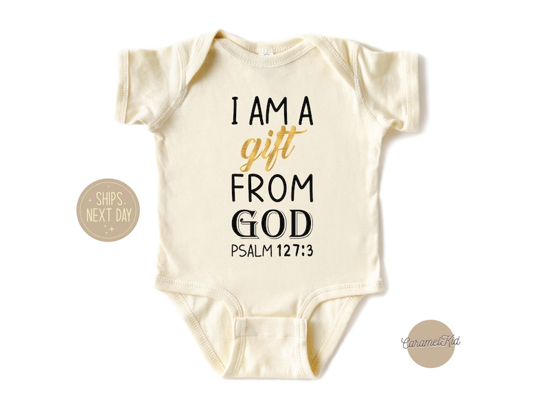 Op de afbeelding: Een cr&egrave;mekleurige baby romper met de tekst "I AM A gift FROM GOD PSALM 127:3" in zwarte en gouden letters.
