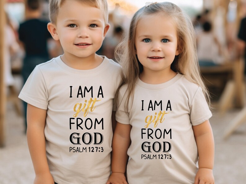 Op de afbeelding: Twee kinderen dragen beige T-shirts met de tekst "Ik ben een geschenk van God Psalm 127:3" in zwarte en gouden letters.