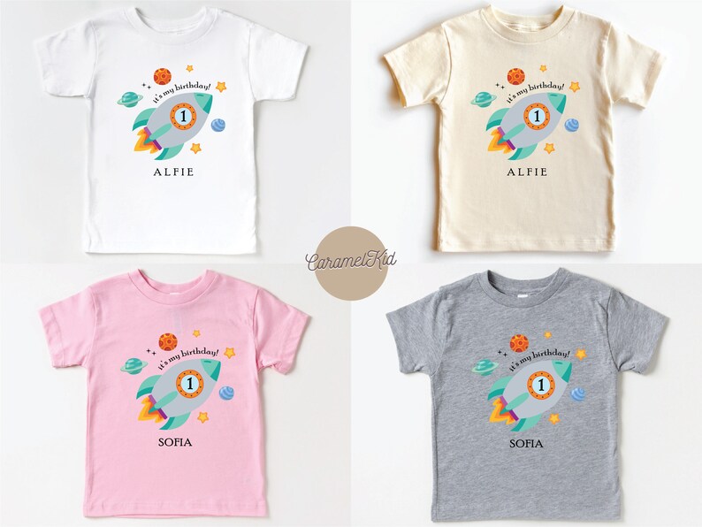 May include: Four toddler t-shirts with a space theme. The shirts are white, beige, pink, and grey. Each shirt features a cartoon rocket ship with the text "It's my birthday!" and a number one. The shirts are personalised with the names "Alfie" and "Sofia".