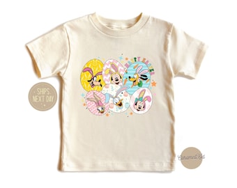 May include: A cream colored t-shirt with a graphic of Disney characters dressed in Easter bunny costumes. The characters are inside of colorful eggs with the text "Happy Easter" above them.