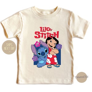 May include: A cream colored t-shirt with a graphic of Lilo and Stitch from the Disney movie. The text "Lilo & Stitch" is in red letters.