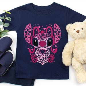 May include: A navy blue t-shirt with a pink and white floral design of Stitch from Lilo & Stitch. The design features hearts and flowers.